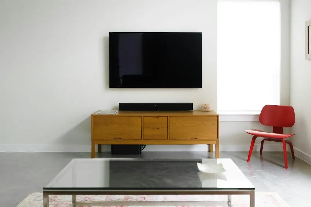 A wall-mounted flat-screen TV above a wooden media console in a white room, the kind of 4K screen MeezzyTV plays on