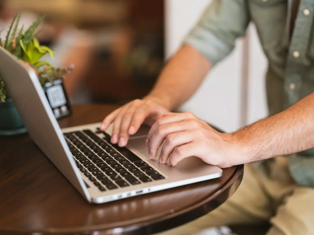 Hands typing on a laptop at a small table, as when comparing the MeezzyTV IPTV price of each plan