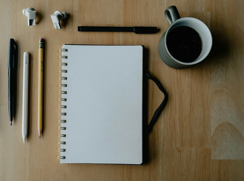 A blank notebook, pens and a cup of coffee on a wooden desk, ready for a checklist to compare IPTV providers